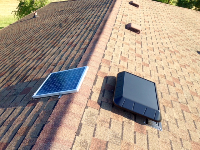 A solar attic vent with a remote panel installed on top of light brown and tan shingles.